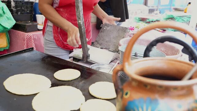 Woman making fresh corn tortillas on a griddle at a market