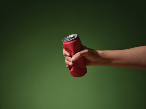 Hand crushing a red soda can against a green background.
