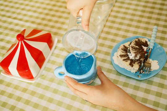 Overhead of female hand pouring water from a glass pitcher into a mug