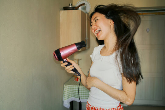 Young asian woman singing into hair dryer during morning routine