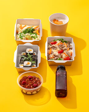 Healthy daily food delivery ration with sushi rice dessert and drink in takeaway containers on yellow background