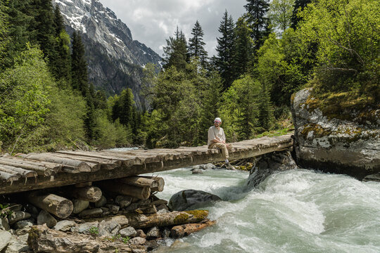 Hiker sitting on a wooden bridge over a glacial river in Svaneti, Geor