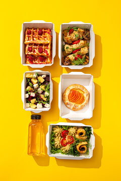 Daily healthy food delivery ration with waffles meat salad pastry and juice in containers on yellow background