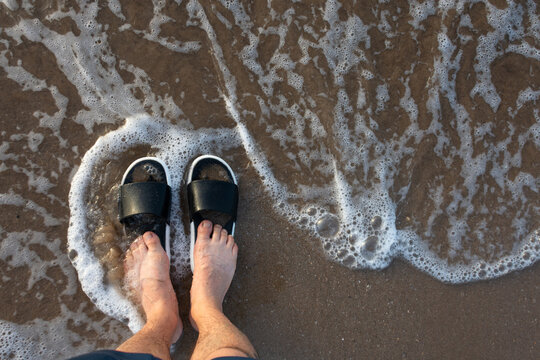 Feet wearing flip flops at the shoreline with gentle waves