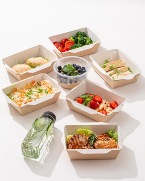 Healthy food delivery containers with grilled steak rice berries salad and detox water on white background