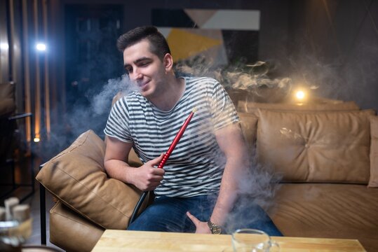 Smiling man surrounded by smoke while holding a hookah hose