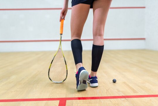 Legs of a female squash player with racket and ball