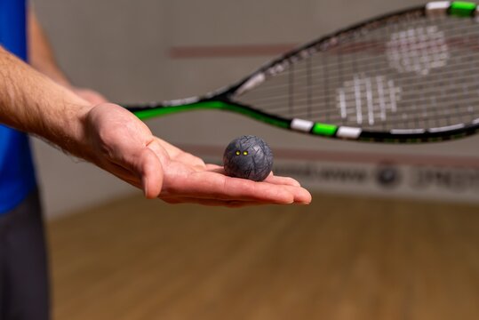 Hand holding a small black squash ball on the court