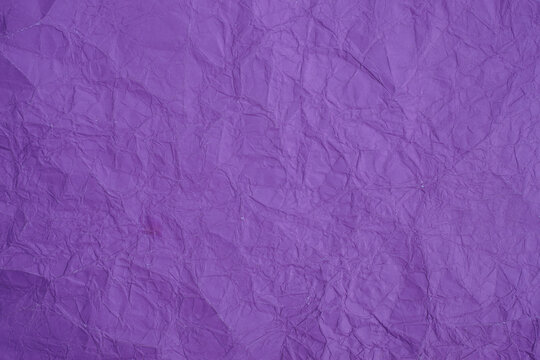 Crumpled purple paper texture with detailed folds, creases, ridges, and natural light and shadow across the surface, creating an abstract textured background