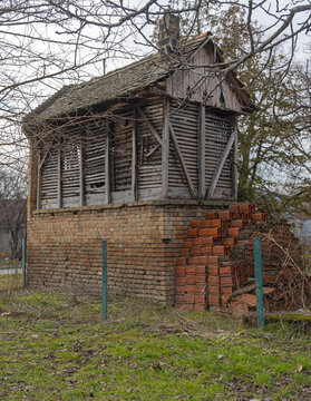 Traditional Serbian Rural Storage Shed With Wooden Upper Section and Pile of Red Bricks Next to Building