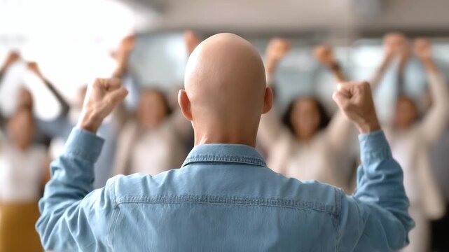 Successful bald man with raised arms celebrating victory with his team in office setting. The concept of motivation, leadership and achieving common goals