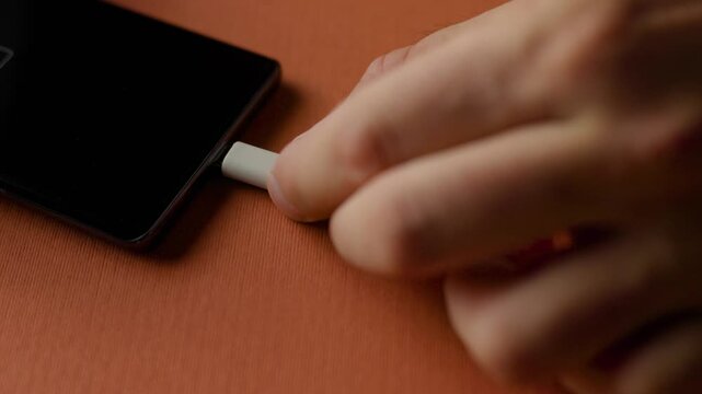 Close up of hand plugging USB-C cable into smartphone for charging