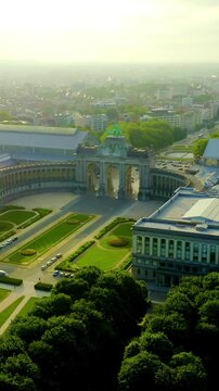 Vertical video. Brussels, Belgium. The Cinquantenaire Arch, a monumental triple triumphal gateway crowned by a bronze quadriga, aerial forward flight over the U-shaped arcade and formal gardens at go