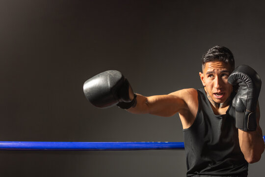 Hispanic boxer throwing powerful punch against dark background