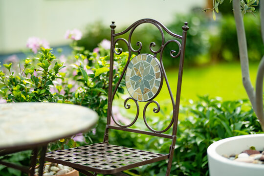 Small table and chairs stand on a wooden garden terrace surrounded by lush greenery and potted plants. Cozy outdoor seating area creates a peaceful summer retreat.