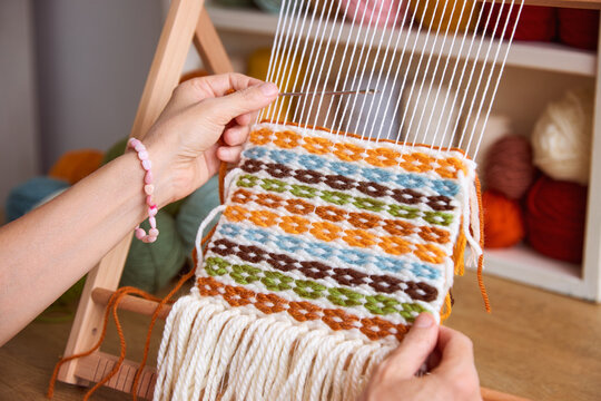 Woman weaving a colorful tapestry on a wooden frame loom using yarn, handmade textile craft