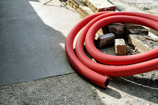 Red corrugated plastic pipe coil on construction site for underground cable protection and utilities installation