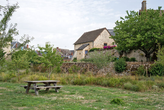 France, Valras Plage August 08, 2026 &mdash; Beautiful stock photograph of a wooden picnic table on a green grass lawn in a scenic French village with traditional old stone houses and lush green trees
