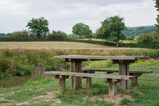 France, Valras Plage August 08, 2026 &mdash; Stock photo of a wooden picnic table with benches on a green grass field near a river bank in a beautiful French countryside landscape on a summer day
