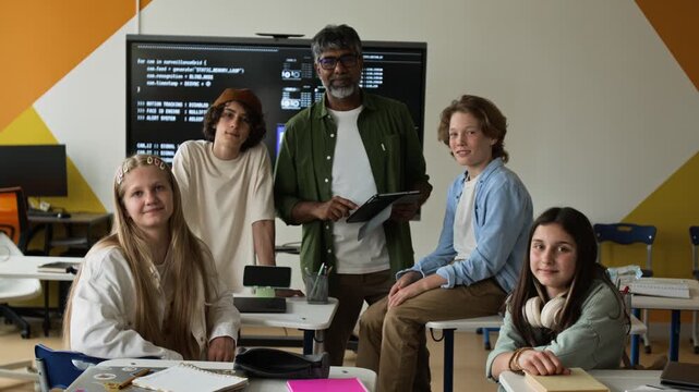 Portrait of middle aged Indian teacher holding tablet and diverse teenagers smiling at camera in coding class, zooming out. Video is perfect for STEM education marketing