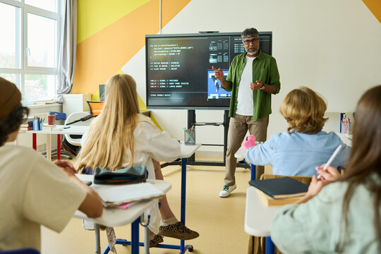 Middle aged Indian teacher explaining coding on interactive screen to diverse teenagers in classroom. Image represents STEM education and ideal for school promotional materials