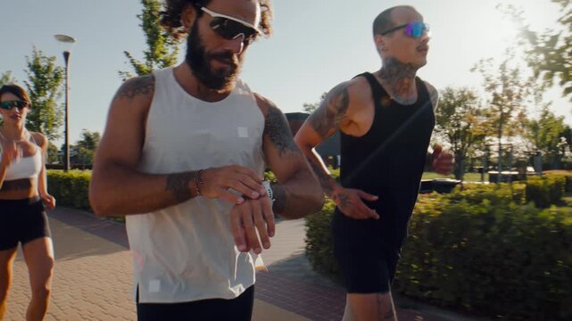 Runners check fitness watches during sunny group park workout