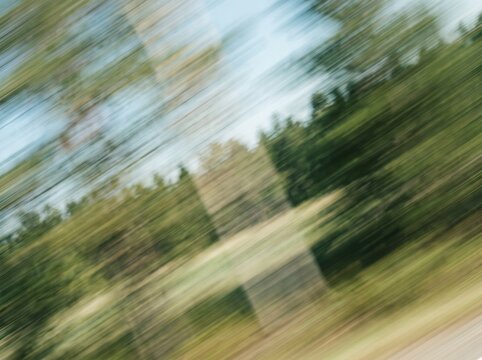 Motion blur landscape view from a fast moving vehicle passing by green trees and fields on a sunny day