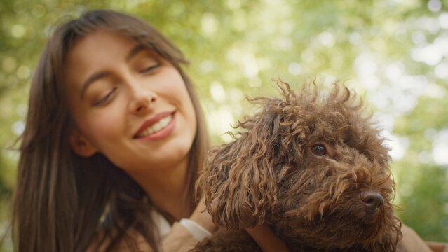 Young woman smiling while holding her fluffy brown poodle in a park