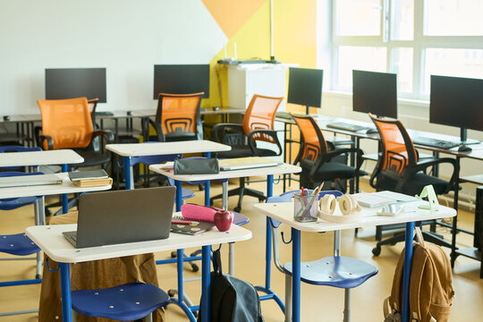 Empty modern classroom featuring school desks with laptops and computer workstations in background. Concept of digital education, suitable for school enrollment marketing campaigns