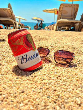 Lloret de Mar Spain August 13 2026 Can of Budweiser beer and sunglasses on the sand at a crowded beach during summer vacation