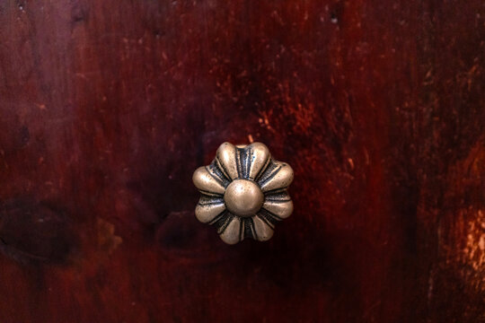 Vintage bronze metal handle knob on antique dark wood furniture drawer, featuring ornate flower detail for classic interior design, home decor, retro wardrobe, cabinet craft, and wooden surface backgr