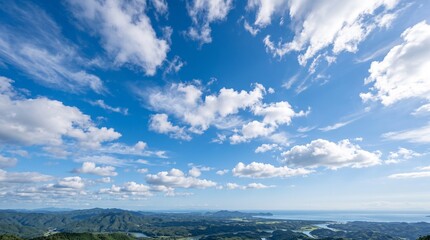 A beautiful natural landscape, with a bright blue sky dotted with fluffy, drifting white clouds. Below, you can see expanses of green mountains, valleys, and the coastline and ocean stretching to the  © Muhammadrizki