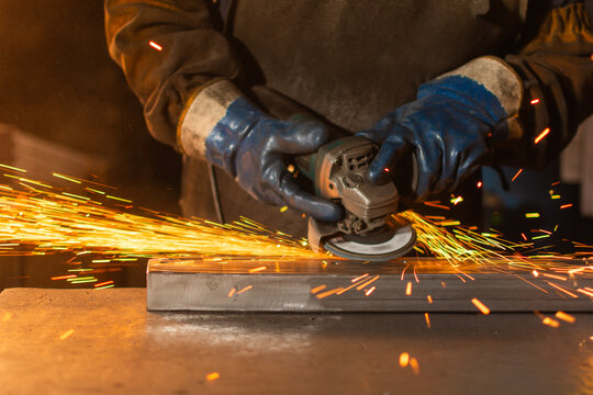 Close up of gloved hands grinding metal with electric grinder and sparks