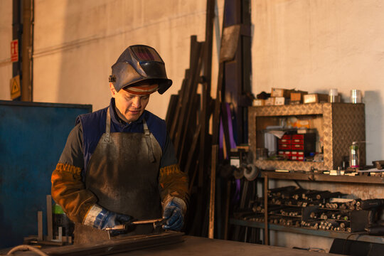Industrial welder preparing metal clamp in workshop with helmet raised