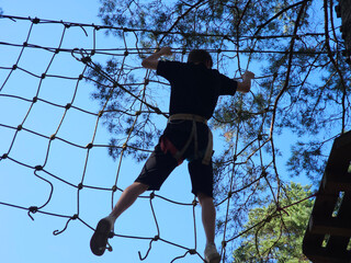Person climbing a rope net on a challenge course © Nadzeya