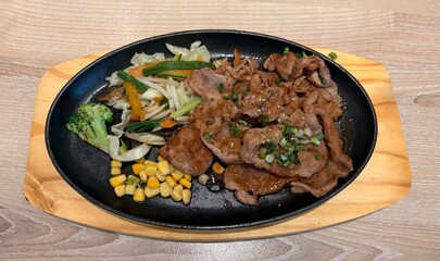Fototapeta premium A sizzling hot plate of stir-fried meat with soy sauce, served with sautéed cabbage, carrots, broccoli, and sweet corn for a savory Asian-style meal.