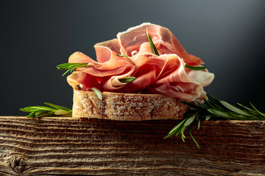 Sandwich with thin slices of Italian dry cured prosciutto, served on an old, weathered board.