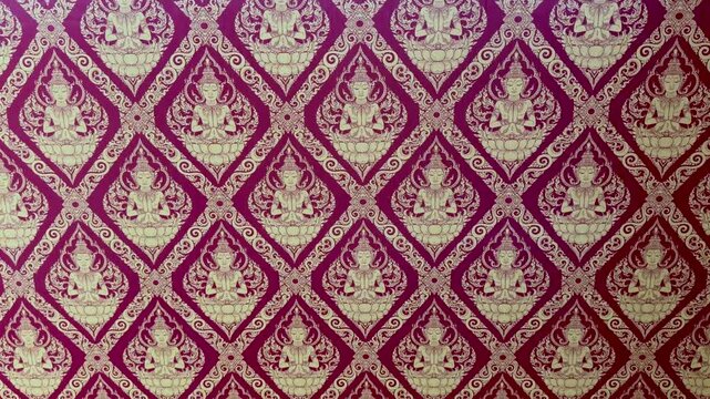 Tilt-up close-up shot of a traditional Thai Kanok pattern with ornate golden deity motifs on a red background.