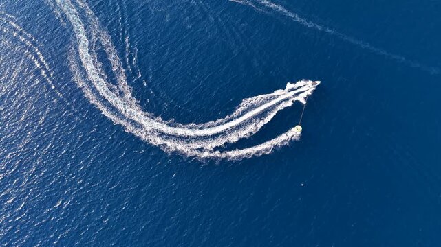 Aerial top down view of motorboat towing yellow inflatable tube ring on blue sea water in Corfu island, Greece