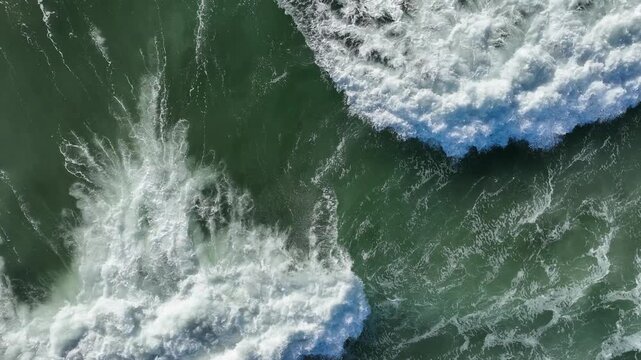 Aerial view of emerald green ocean waves crashing onto a sandy beach, with white sea foam swirling across the water capturing the raw power and natural beauty of the coastline.