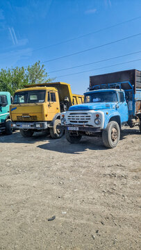 Classic Soviet trucks: a blue ZiL-130 and a yellow Kamaz-5511 dump truck parked in the sunshine near Tbilisi; historic commercial vehicles, Georgia 11.4.25