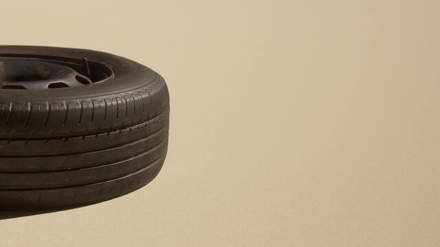 A tire rests on a sandy surface. The background shows soft light and vague shapes. There are no people or other objects nearby. The scene captures a quiet moment in an open area.