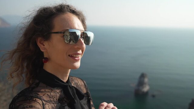 Woman selfie travel. Happy female tourist waving and recording video on mountain cliff overlooking the blue sea.