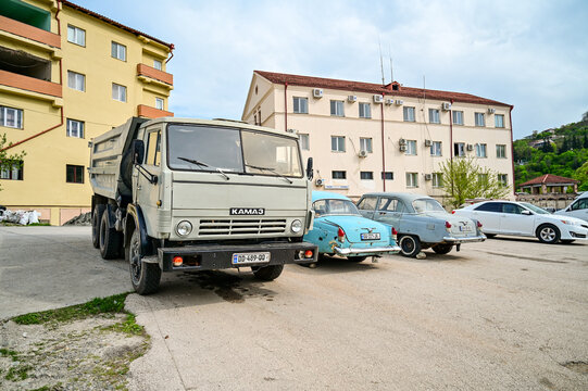 A gray KamAZ-5320 truck is parked next to a light blue GAZ-21 Volga classic car from the 1950s on a residential street in Sighnaghi; historic Soviet vehicles, Kakheti region, Sighnaghi, Georgia 12.4.2