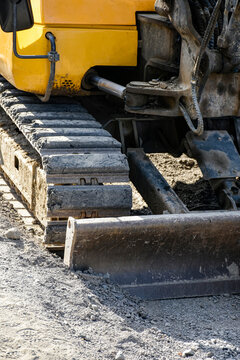 Close up of yellow excavator continuous track and front dozer blade on construction site ground