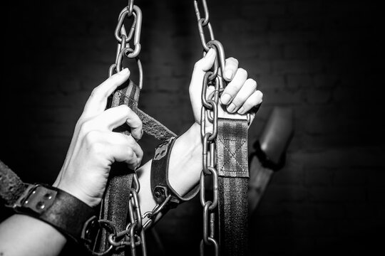 Dark chains grip hands bound in leather restraints