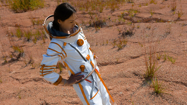 Confident female astronaut in an orange trimmed spacesuit surveying a red desert plain