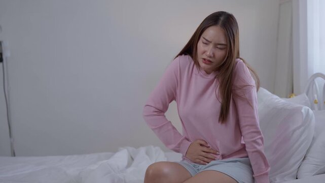 Abdominal pain concept, woman holding stomach while sitting on bed at home, suffering cramps and discomfort, abdominal pain, menstrual cramps, stomachache, food poisoning, illness
