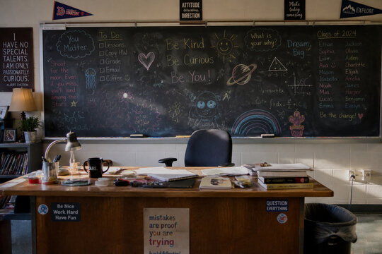 Classroom chalkboard covered in colorful doodles with messy desk.