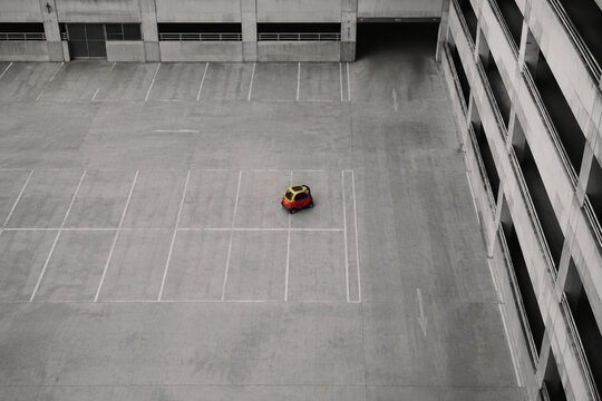 Aerial view of tiny colorful microcar in vast concrete parking garage.